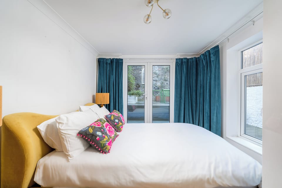 Relax in this stylish and inviting bedroom featuring a plush mustard-colored headboard, crisp white linens, and vibrant decorative pillows for a touch of personality.