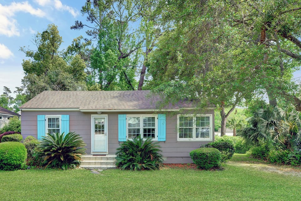 Front Exterior With Coastal Shutters - 204 Ashantilly Avenue makes a bold first impression with bright blue shutters, a wide front yard, and classic St. Simons Island charm—just minutes from the beach.