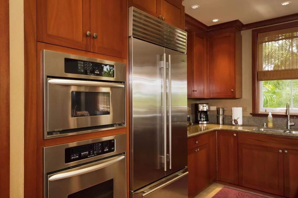 Close-up view of double ovens and stainless fridge in a well equipped, upscale kitchen design.

