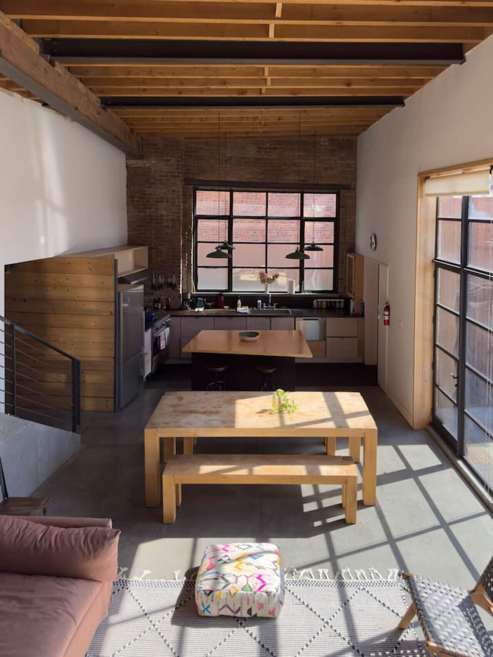 Expansive, sunlit living and dining area with industrial-style windows and warm wood accents.