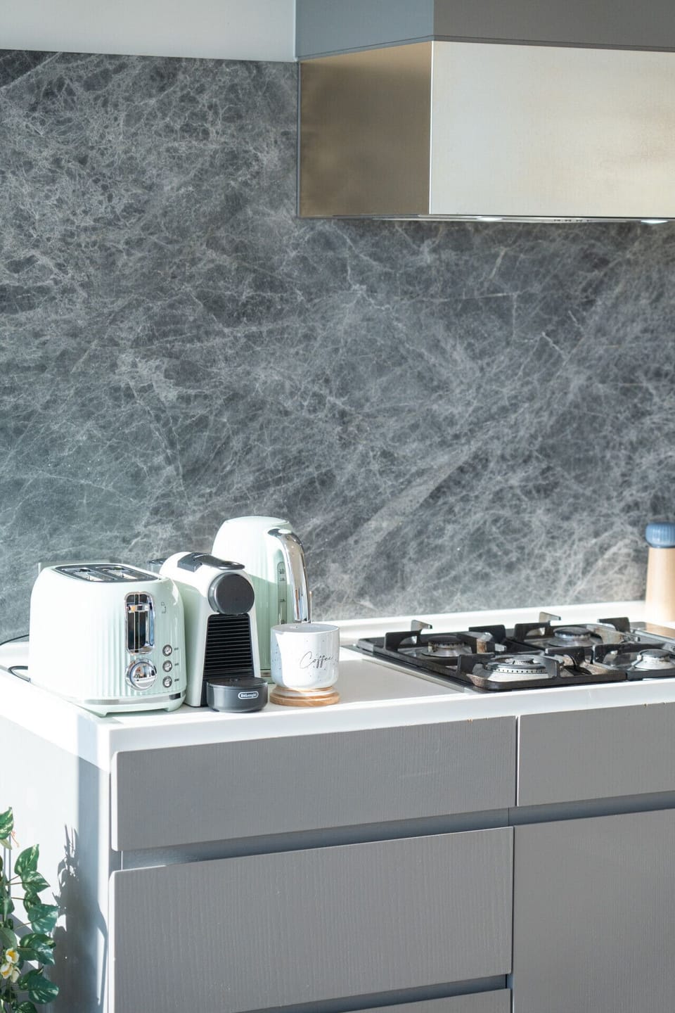 A well-equipped kitchen bench with a Nespresso machine, toaster, and gas cooktop set against a dramatic dark marble splashback. Everything guests need for a relaxed morning routine is within easy reach.