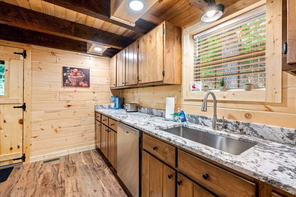 This kitchen corner offers all the essentials: toaster, Keurig, dishwasher, and spacious prep areas—plus a window view of the woods beyond.