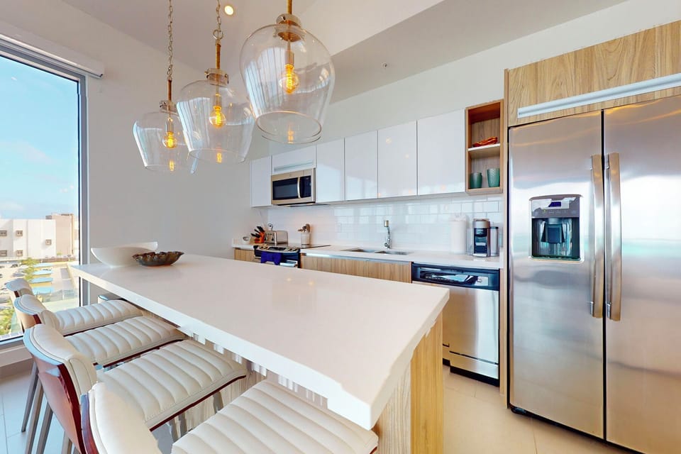 Your modern, sunlit kitchen is fully equipped with sleek appliances and a spacious island—perfect for whipping up meals while enjoying ocean glimpses through the window.