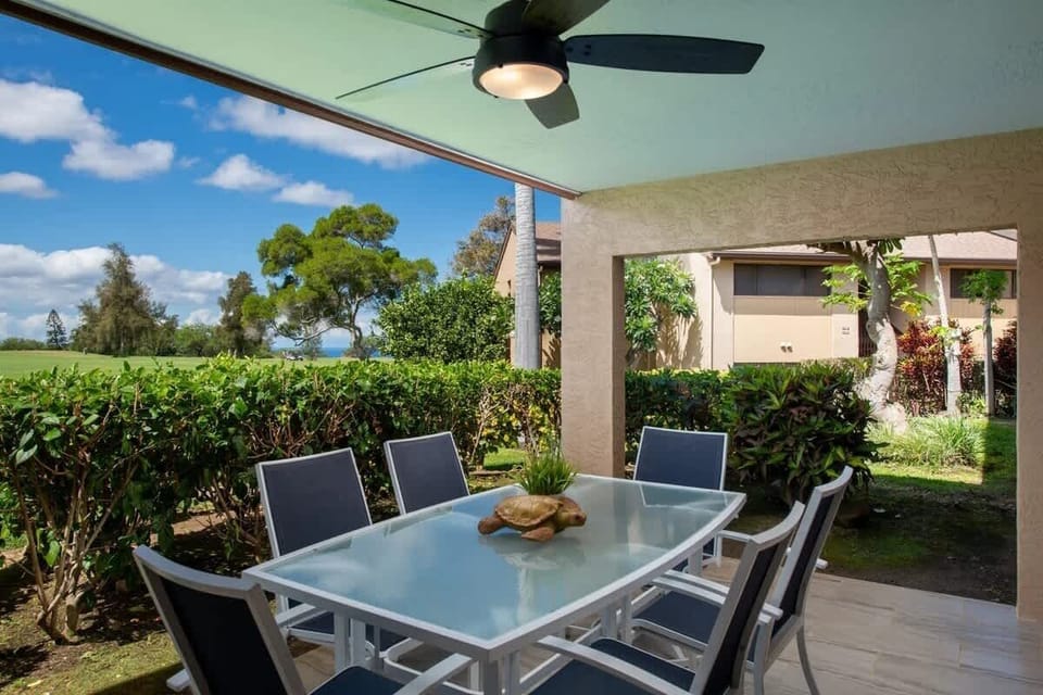 Covered lanai features sleek dining setup with views of greenery and golf course in the distance.

