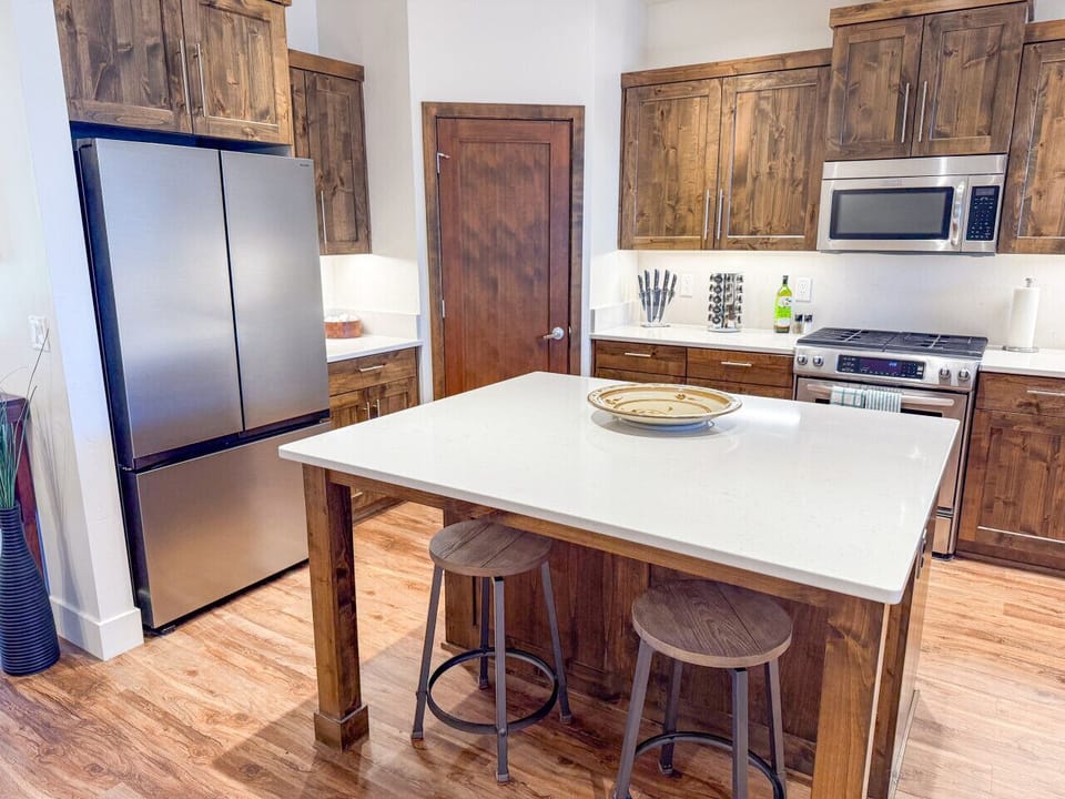 Fully equipped kitchen featuring rich wood cabinetry, stainless steel appliances, and a spacious quartz island—perfect for preparing meals or gathering with family and friends.