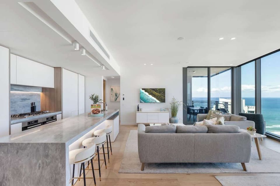 Open-plan luxury kitchen and living area bathed in natural light from soaring 2.85m floor-to-ceiling glass windows.