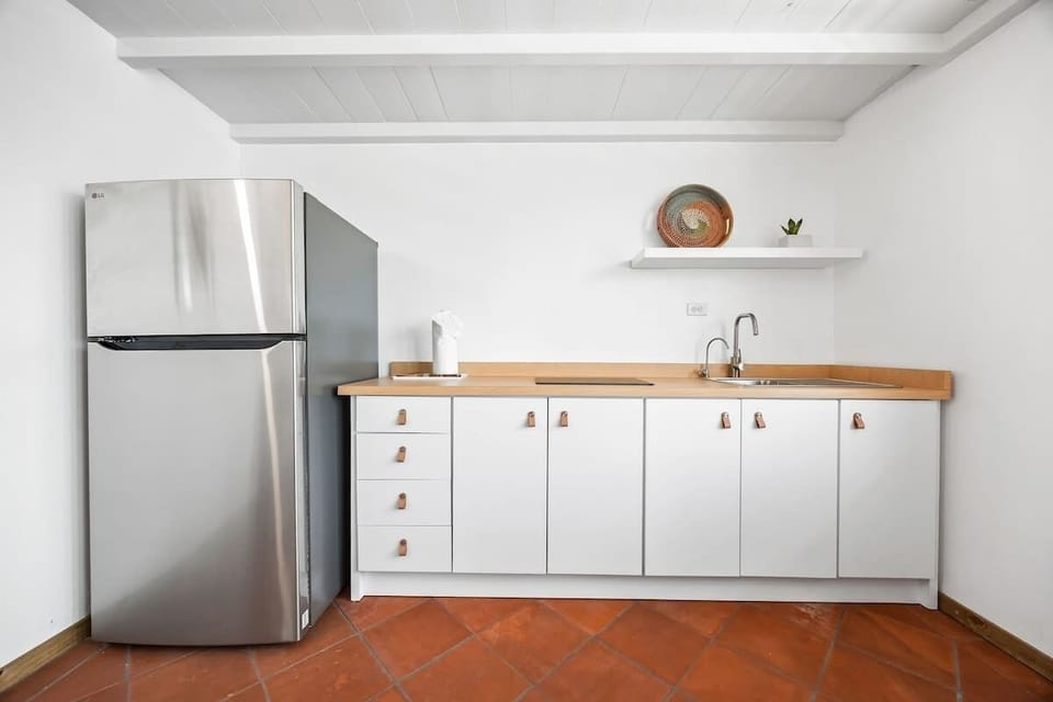 This efficient kitchenette features modern white cabinetry with sleek hardware, a practical countertop, and a full-sized stainless steel refrigerator. Perfect for convenient meal prep.