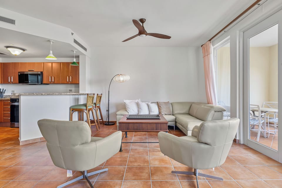 livingroom wiht large sofa, seats, ceiling fan, airconditioner, balcony with views,  lamp, open kitchen with countertop, fridge, microwave, oven, kithchen cabinets, floor lamp, coffee table