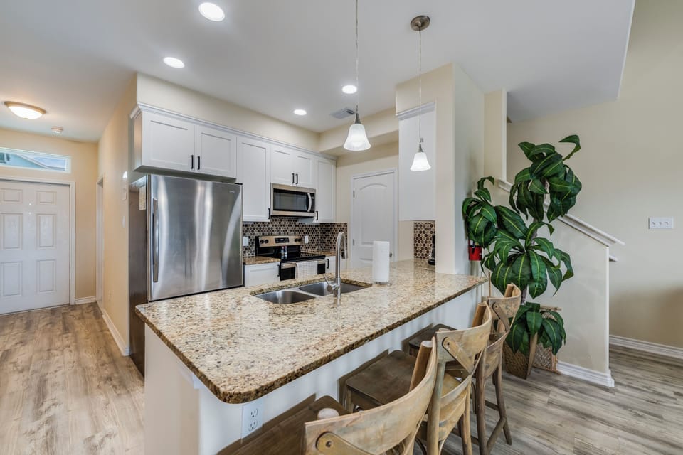 Prepare your favorite meals in this bright, fully equipped kitchen featuring modern stainless-steel appliances, granite countertops, and a welcoming island with bar seating for casual dining.