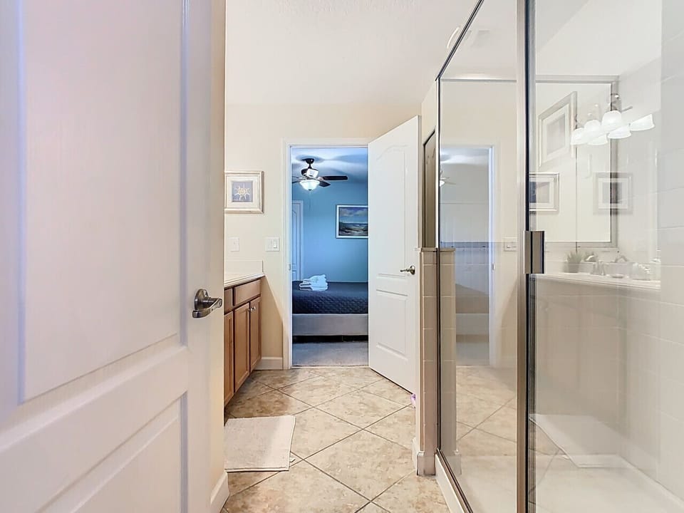 Bright bathroom with glass shower and vanity, leading into the bedroom.