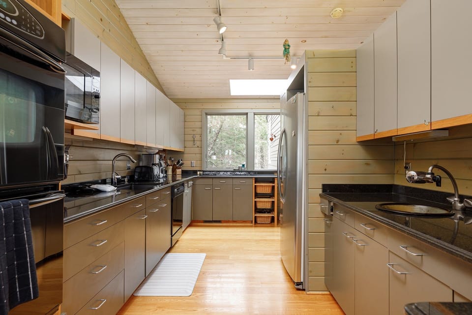 Prepare meals with ease in this well-equipped kitchen, offering a view into the living room and natural light from the window. The bar area is perfect for casual dining or chatting with the cook.