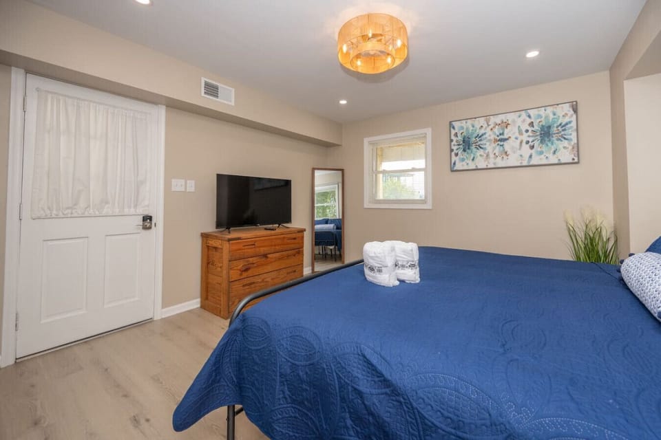 Cozy king bedroom with soft coastal décor, plush navy bedding, a flat-screen TV, and warm lighting, ideal for relaxing after a fun day at the beach.