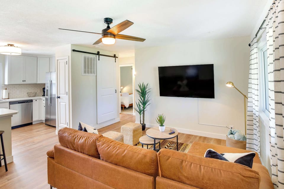 Large windows brighten the space with natural light, and the ceiling fan with a dim light sets the perfect evening vibe. Lush indoor plants, an accent lamp, and a sleek center table complete this inviting space, ideal for couples, solo travelers etc.