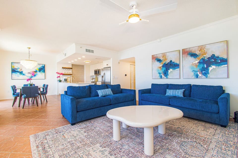 Sink into plush blue sofas in your spacious living area, where coastal artwork and modern comfort create the perfect retreat for relaxation and stunning sunsets.