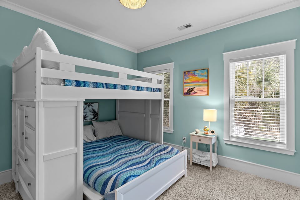 Light blue room, bunk bed, wall TV, window blinds, nightstand, lamp, beach art, carpet floor, bright coastal style.