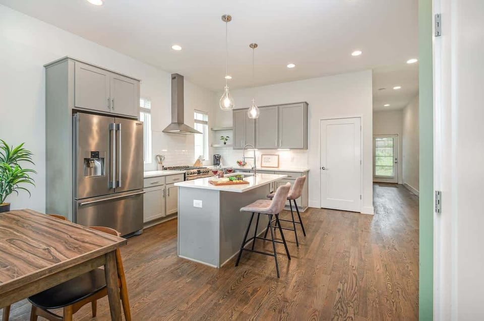 Unit 1: Bright open-concept kitchen featuring a quartz-topped island with bar seating, stainless steel appliances, and abundant natural light streaming through the windows.