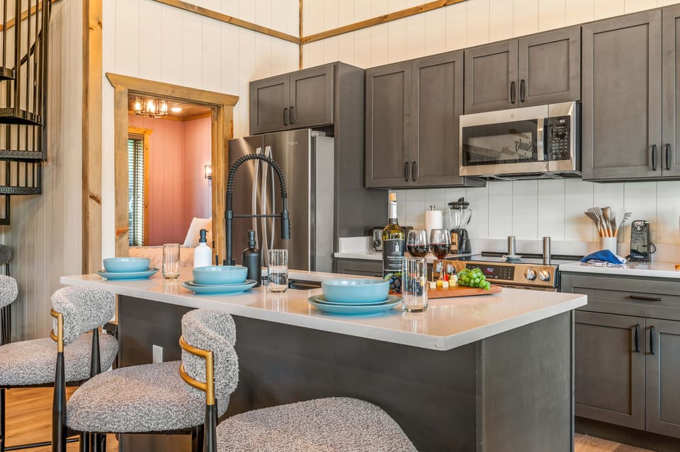Modern kitchen with dark cabinets, white island bar seating, and spiral stairs.