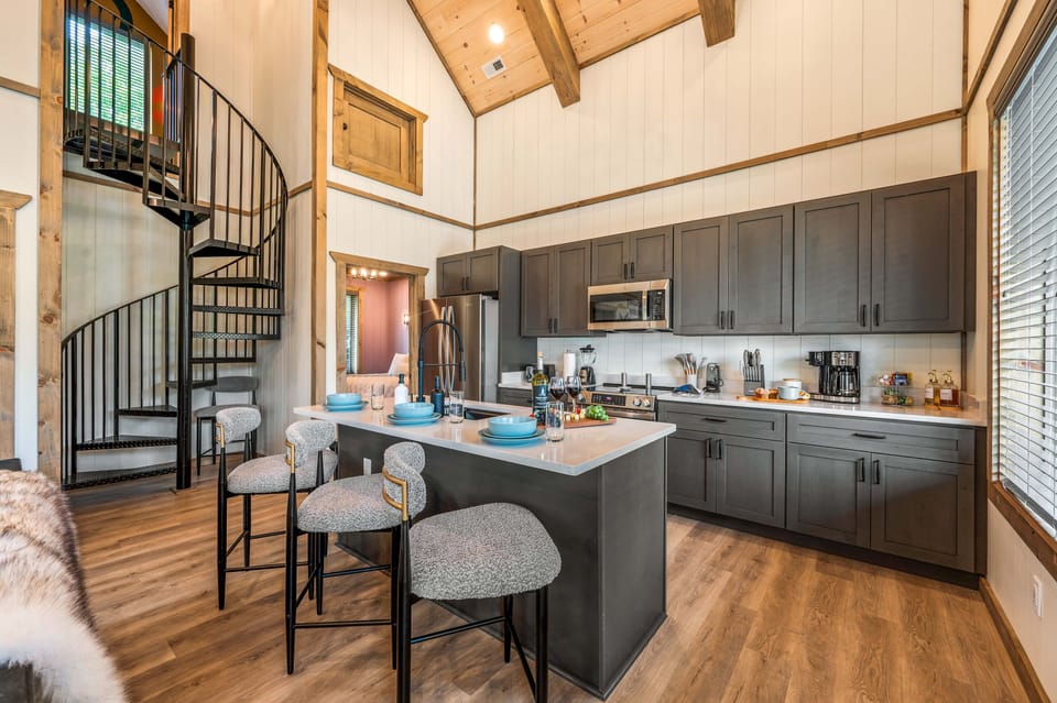 Modern kitchen with dark cabinets, white island, bar stools & spiral staircase.