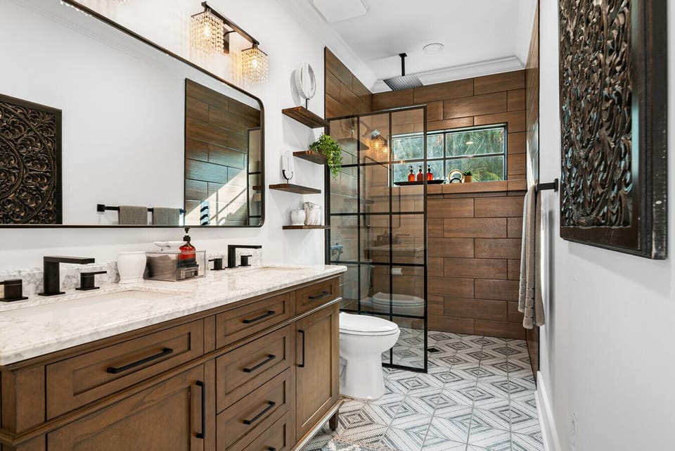 Sunlit bathroom with dual-sink marble vanity, wood-tile walk-in shower, and geometric floor tile