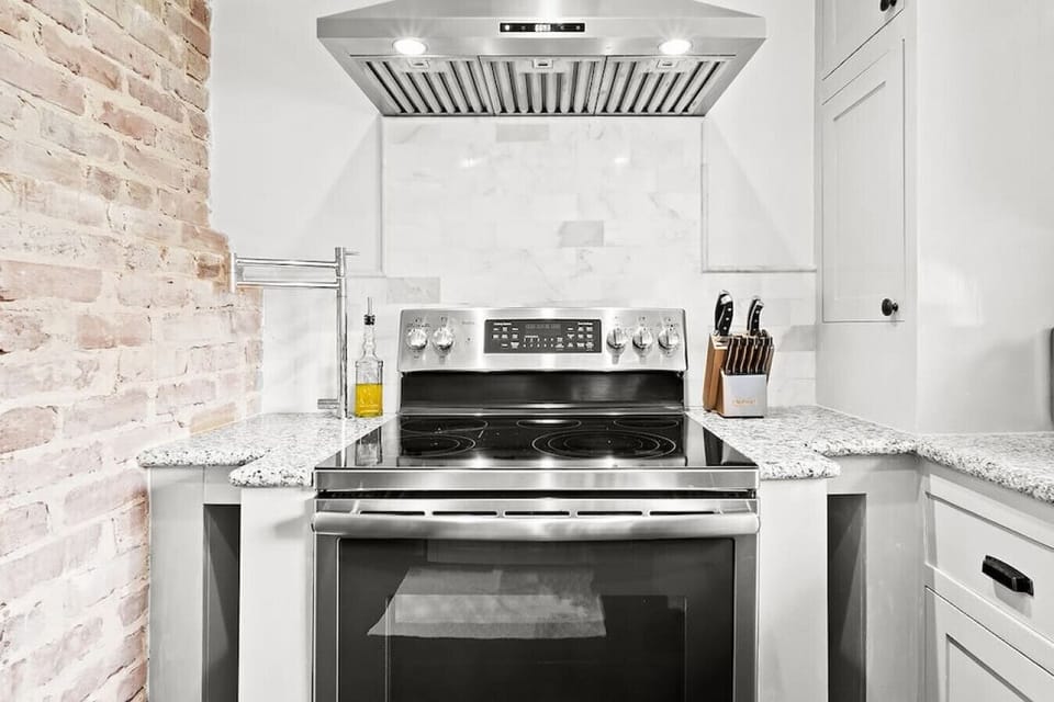 Contemporary kitchen highlights stainless steel appliances and a sleek range hood against white cabinetry and a textured backsplash.
