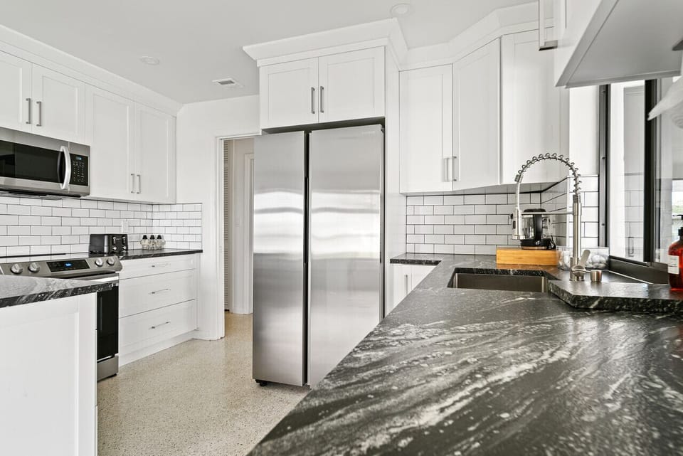 Bright and modern kitchen offers white cabinetry, stainless steel appliances, and a spacious dark countertop with a stylish faucet.
