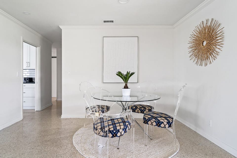 Bright dining nook features a round glass table with stylish patterned chairs and a decorative sunburst on the wall, creating a cozy eating space.
