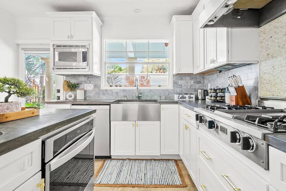Modern kitchen showcases sleek white cabinetry, stainless steel appliances, and a dark countertop with a view from the window.
