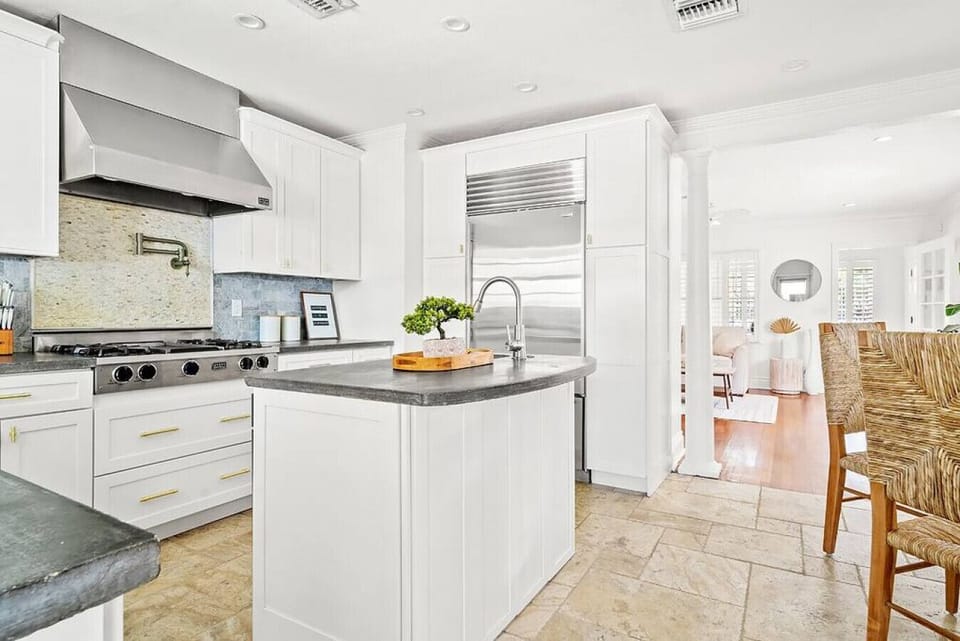Modern kitchen boasts sleek white cabinetry, stainless steel appliances, and a view into a bright dining area.

