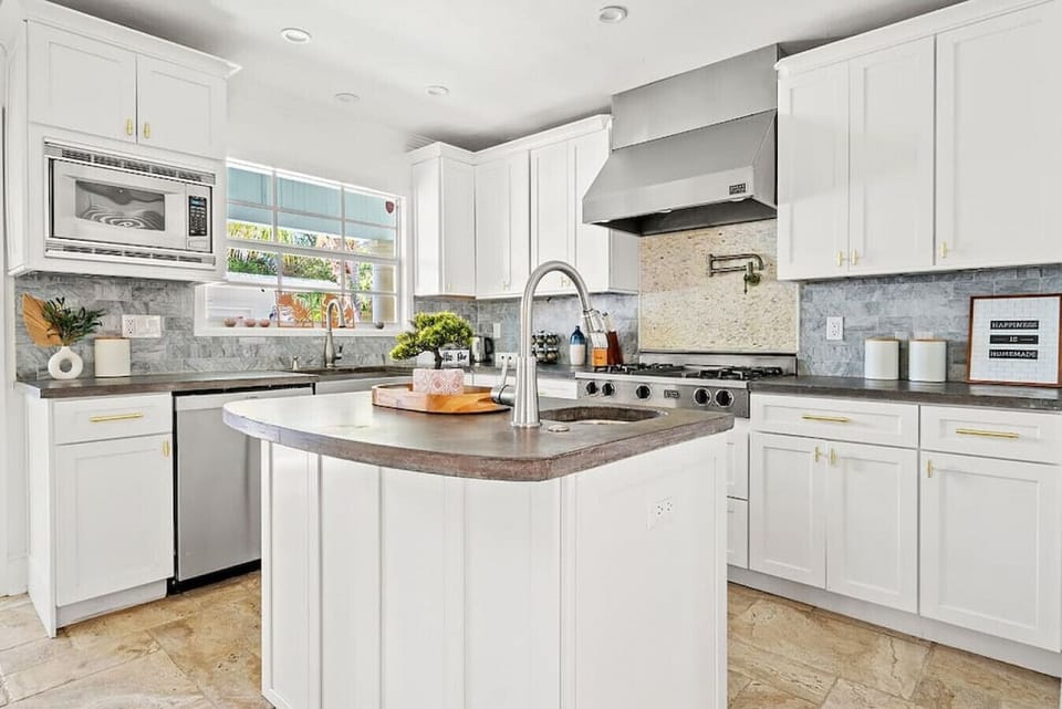 Bright and modern kitchen offers white cabinetry, stainless steel appliances, and a spacious island with seating.
