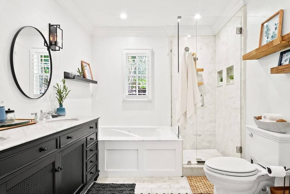 Modern bathroom offers a sleek black vanity, a round mirror, and a combination tub and shower with white tiling.
