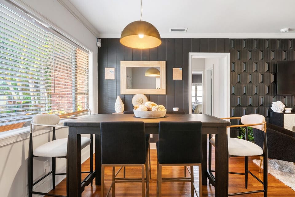 Modern dining area features a long dark wooden table with stylish chairs under a warm pendant light, with a glimpse into the kitchen.
