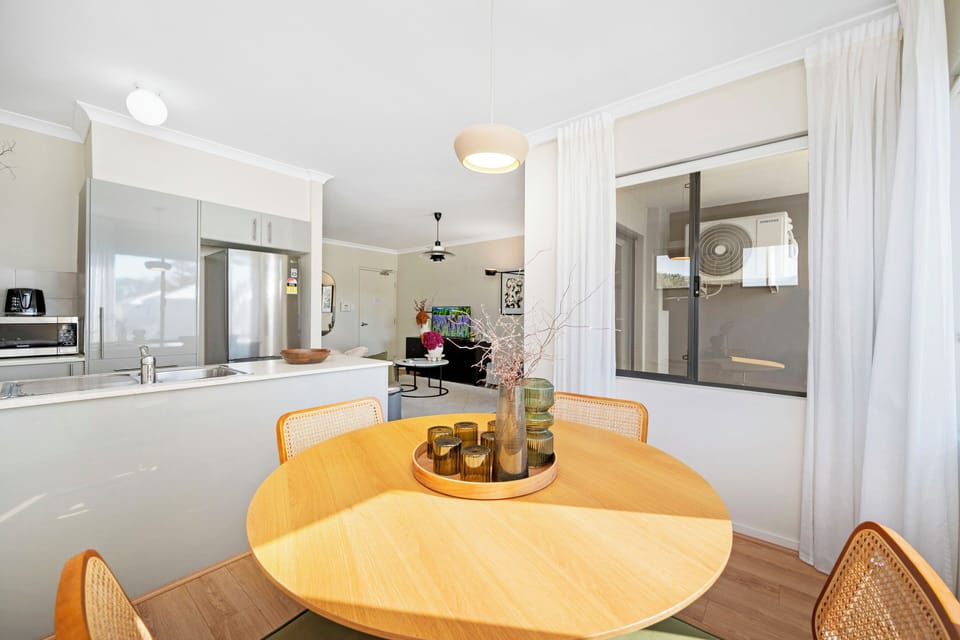 Dine casually in a bright space featuring a round wooden table and comfortable chairs, with a view towards the modern kitchen, perfect for enjoying meals and conversation.