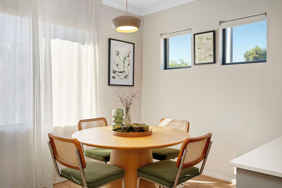 Enjoy intimate meals in a charming dining area featuring a round wooden table and chairs, set against a bright window with soft curtains, offering a delightful spot for dining.