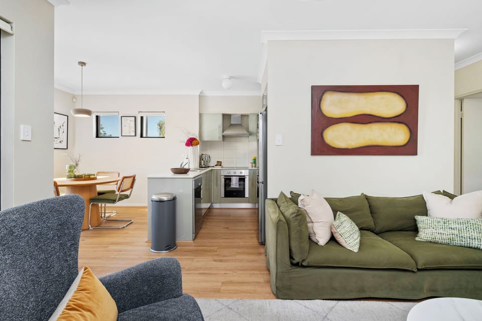 Experience open-plan living in a connected space featuring a welcoming living area with a green sofa, a dedicated dining area, and a well-equipped kitchen, ideal for modern lifestyles and social gatherings.