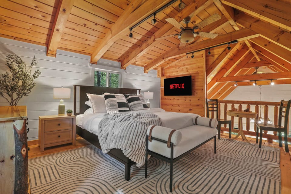 Loft bedroom with king size bed, 50" smart TV, bistro table for coffee or a board game, dresser, portable fan, overhead fan, and an ottoman.