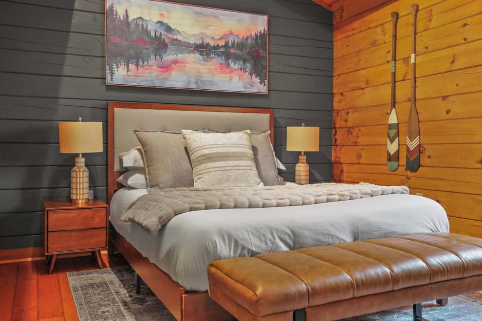 Queen bed with smart TV, clothing storage, ottoman, curtains, and portable fan.