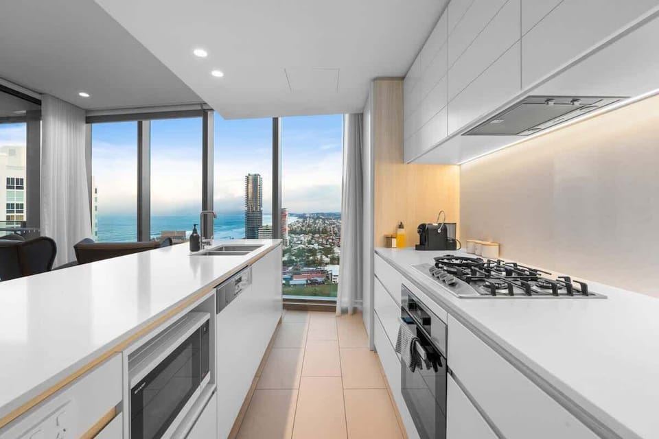 Cooking with the view — Long island bench with stone splashback, LED lighting, and quality European appliances including a microwave, fridge, oven, and gas cooktop.