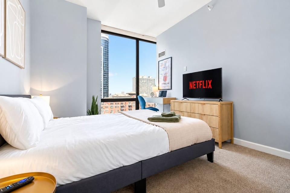Bright modern bedroom with city views, desk space, and TV entertainment