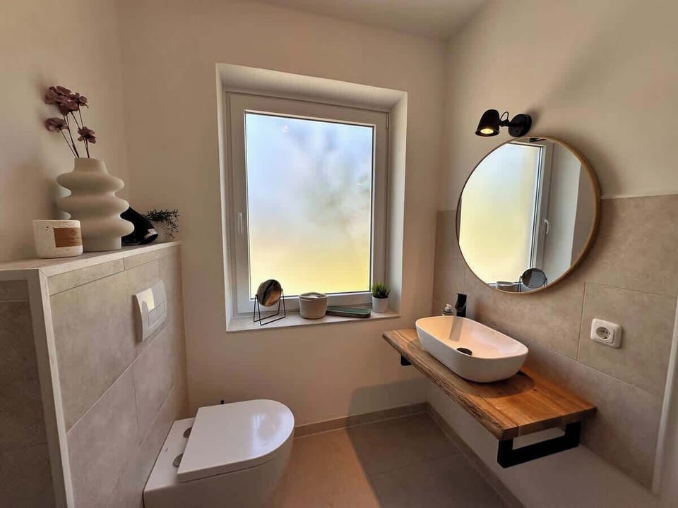 Helles Badezimmer mit Dusche, WC, großem Spiegel und Fenster. 