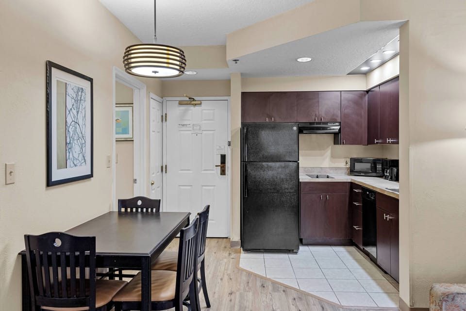 Welcome to a cozy kitchen and dining area, where dark wood cabinetry and sleek appliances blend warmth with functionality. Savor meals at the black dining set, surrounded by soft lighting that enhances the inviting atmosphere.