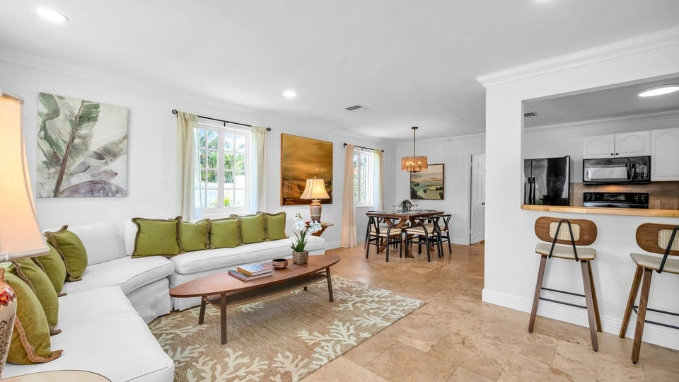 This bright and airy living room offers plenty of space for up to 6 guests to relax in comfort. Featuring a wraparound sectional with plush green accent pillows, a smart TV, and tasteful tropical decor, it's the perfect place to unwind after exploring WPB