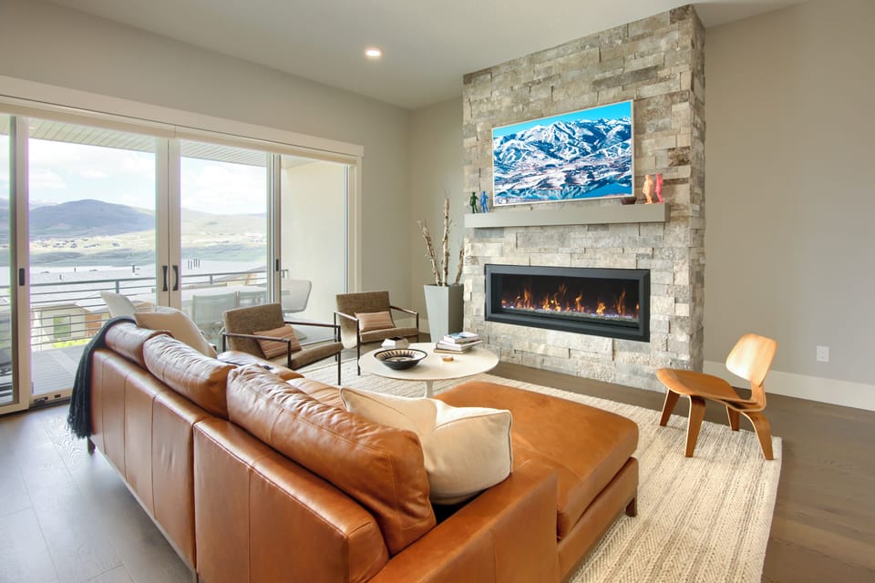 Bright living room with leather seating, stone fireplace, and mountain views through large windows.