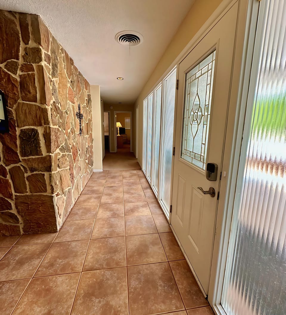 Welcoming entry hallway with elegant tile flooring, a beautiful stone accent wall, and a decorative glass front door.