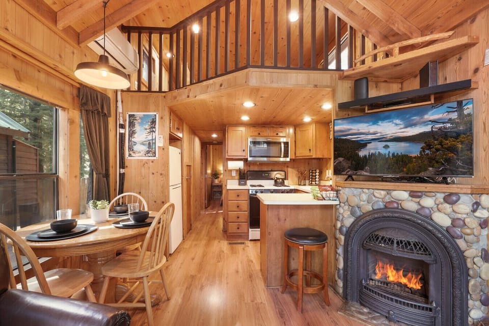 Cozy up in the cabin’s inviting living room—featuring a fireplace, TV, AC mini split, and large windows that frame the towering pines and let in the crisp mountain air. Step right out onto the patio for fresh forest views.