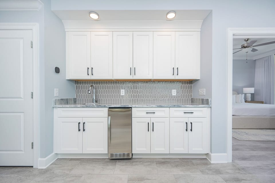 Pour a drink from the wet bar featuring sleek cabinetry, stylish backsplash, and elegant countertop
