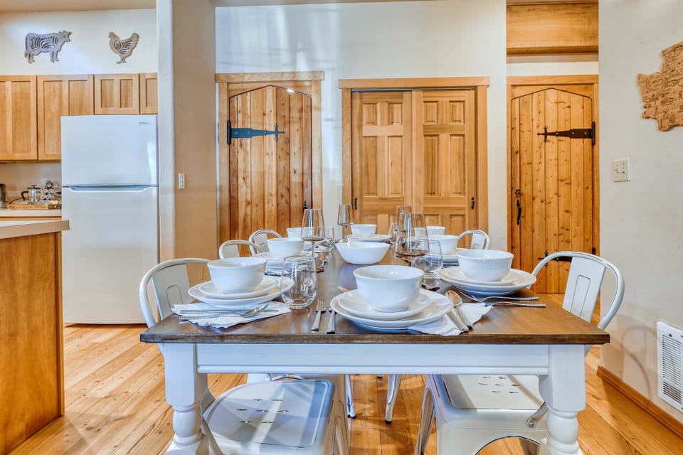 A warm, inviting dining space with a solid table that comfortably seats 8 guests, perfect for family meals or group gatherings. Natural light streams in from nearby windows, highlighting the rustic décor. CB1