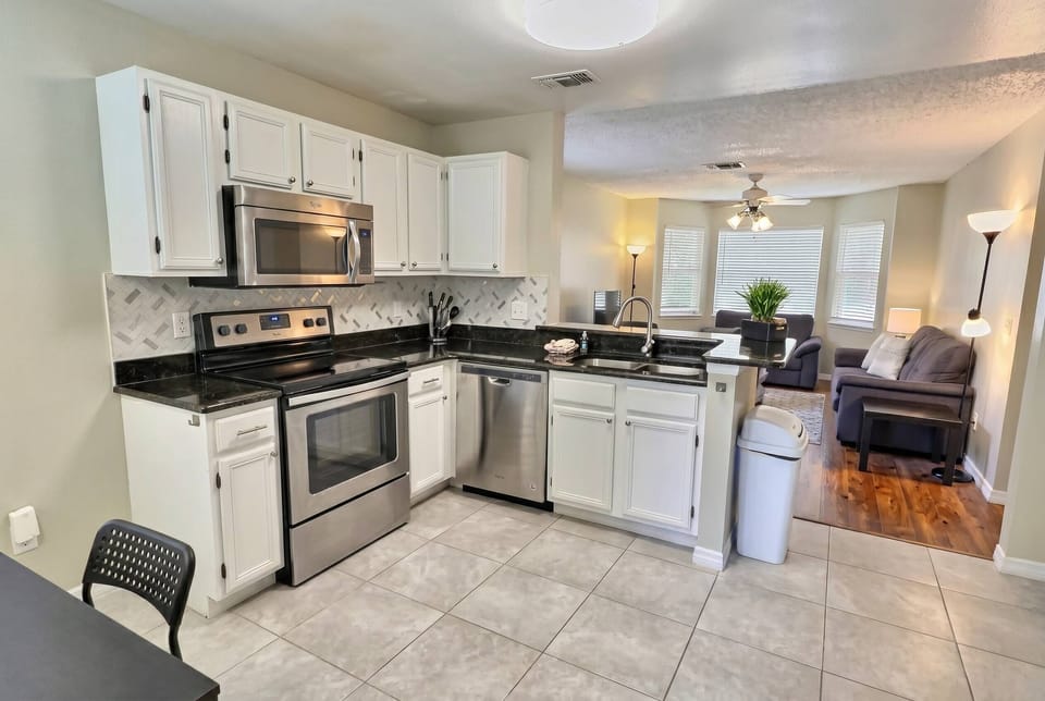 This bright kitchen boasts sleek black countertops and white cabinetry, offering a fresh, functional space. Enjoy modern appliances and an open layout that connects to a cozy living area, ideal for meals and gatherings.