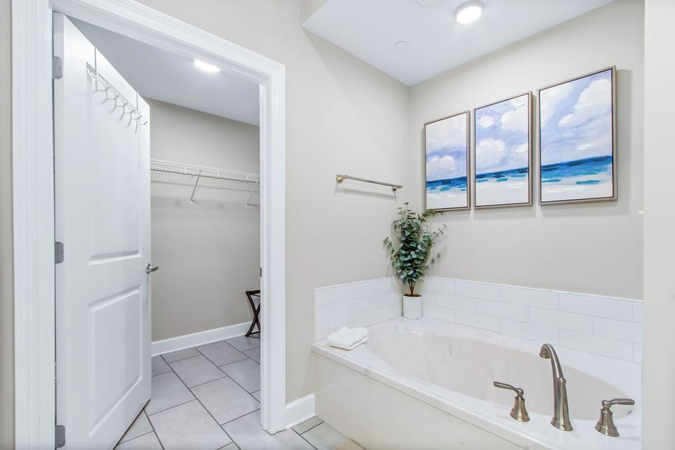 Elegant master bathroom featuring a spacious tub, artwork that enhances the relaxing vibe, and large walk-in closet