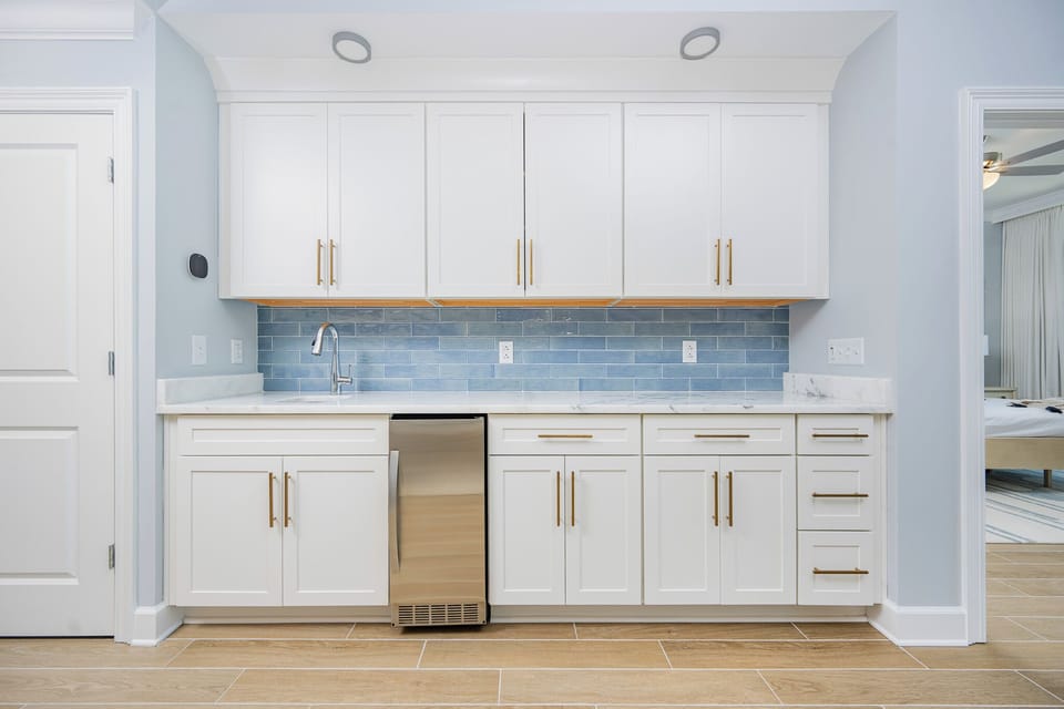 Prepare snacks and drinks at the wet bar featuring sleek cabinetry and a soothing blue backsplash