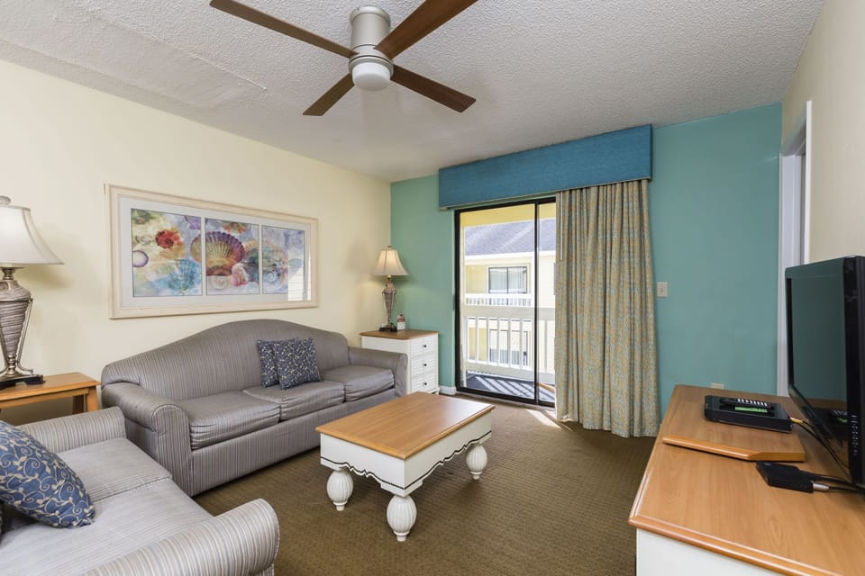 The inviting living room features comfortable seating and a private balcony, ideal for enjoying your coastal retreat.